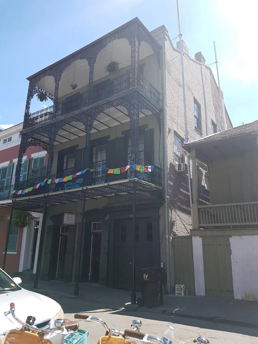 The image shows a traditional two-story building with wrought-iron balconies a few colorful flags hanging between the floors under a clear sky capturing a hint of the charming architectural style seen in places like the French Quarter of New Orleans