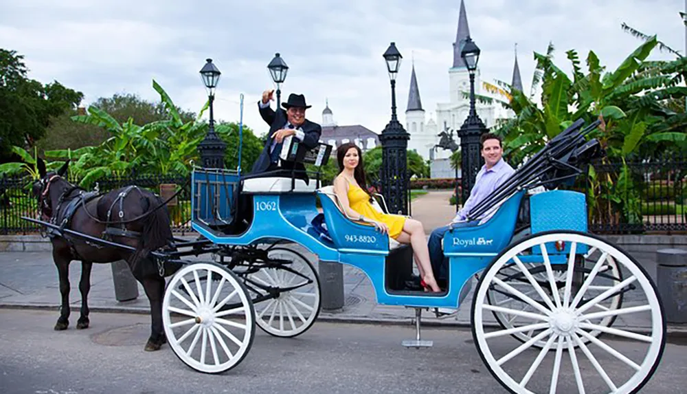 A man and a woman enjoy a carriage ride with the driver tipping his hat in front of an elegant gated area with historic architecture in the background