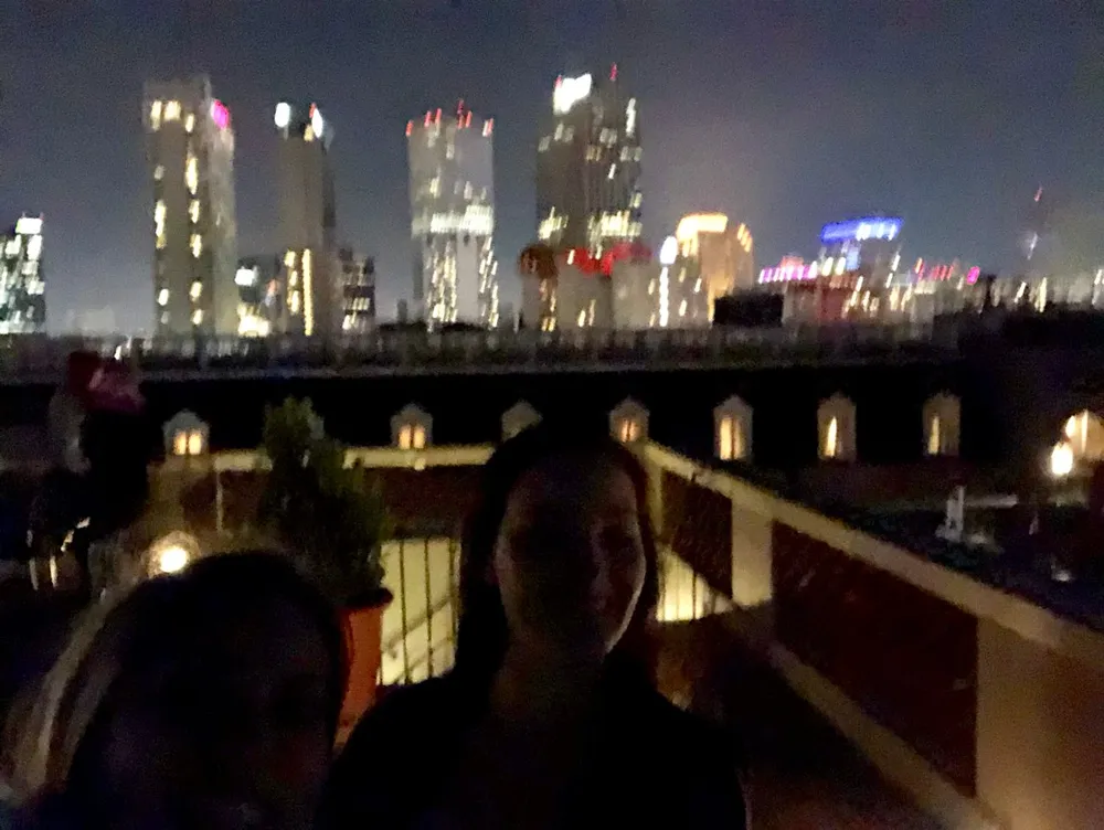 This image shows two people posing for a blurry night photograph with city lights in the background