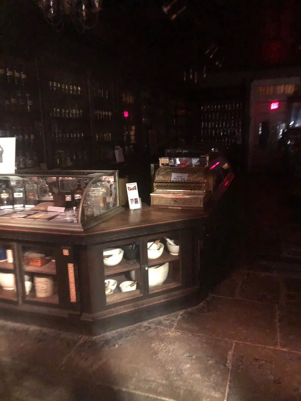 The image depicts a dimly lit interior possibly a vintage or old-fashioned shop or apothecary with shelves full of bottles and a counter showcasing various items