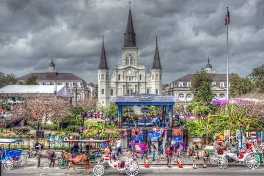 The photo depicts a vibrant street scene with horse-drawn carriages in the foreground and the iconic St. Louis Cathedral in the background, likely in New Orleans' French Quarter.