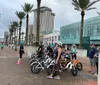 A group of people with bicycles wearing helmets are gathered on an urban waterfront promenade possibly preparing for a ride or tour