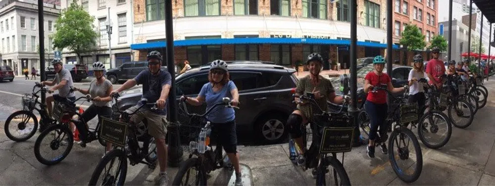 A group of people wearing helmets are standing with their bicycles on a city street ready for a biking activity