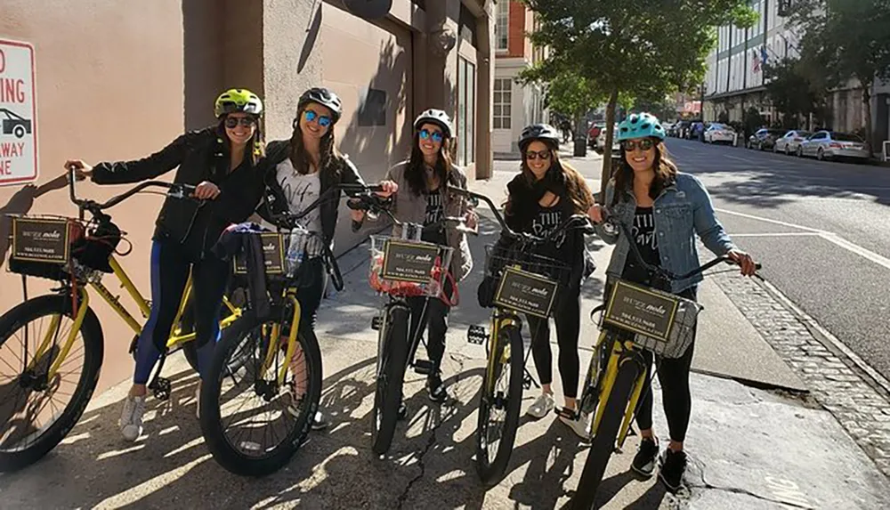 A group of five smiling people wearing helmets are posing with rental bicycles on a sunny city street