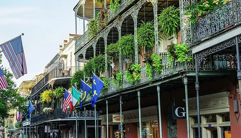 The image shows a picturesque street lined with historic buildings featuring ornate ironwork balconies adorned with lush green plants and various flags evoking the charming atmosphere of New Orleans French Quarter