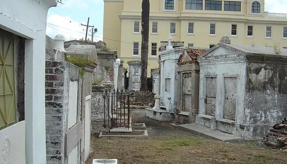 The image shows an old cemetery with above-ground tombs and worn-out gravestones with a yellow building in the background