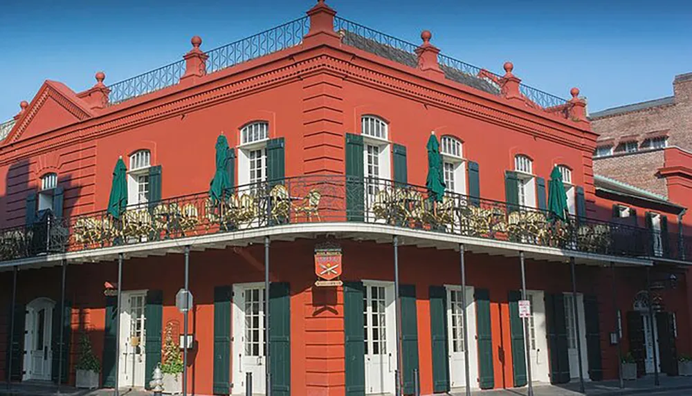 The image depicts a vibrant red building with a second-story balcony adorned with intricate ironwork characteristic of New Orleans French Quarter architecture