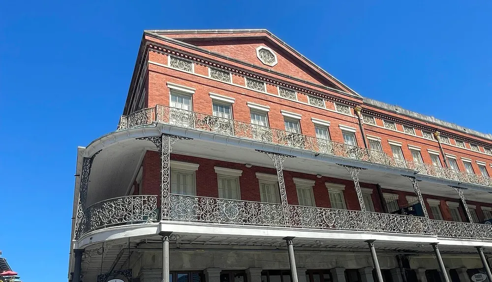 The image shows a corner view of a stately red brick building with intricate black ironwork balconies under a clear blue sky