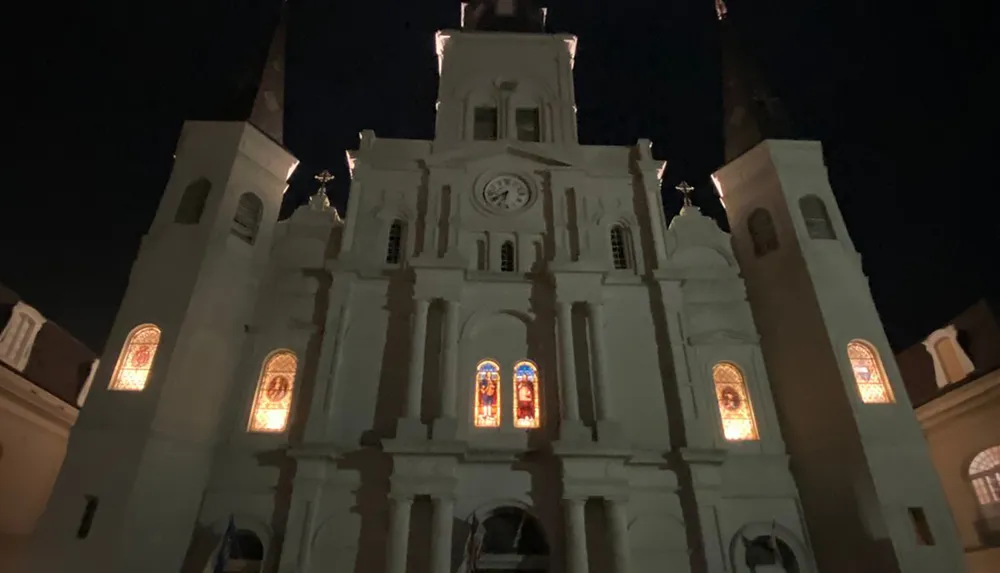The image shows a well-lit facade of a grand building presumably a church with illuminated stained glass windows captured against a dark night sky