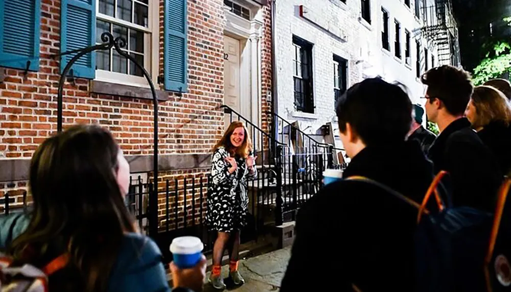 A group of people listens to a woman who appears to be giving a tour or talk outside a historic building at night