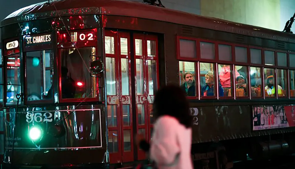 A vintage streetcar marked St Charles is illuminated at night with passengers visible through its windows