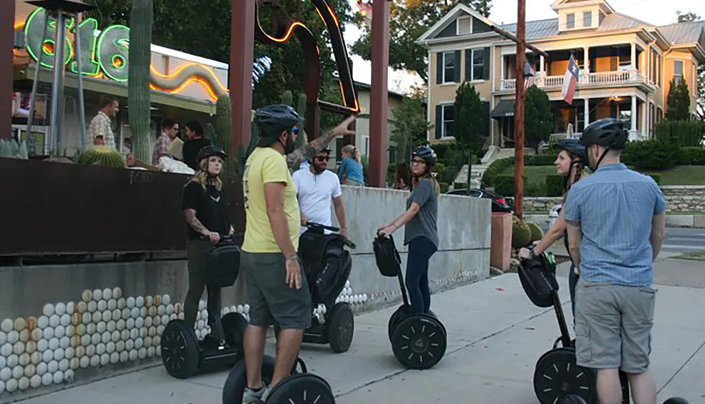 A group of people wearing helmets are riding Segways on a city street with a restaurant in the background
