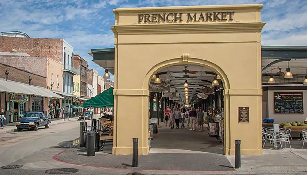 An arched entrance with the sign FRENCH MARKET leads to a bustling outdoor market with shops pedestrians and seating areas under an extended roof