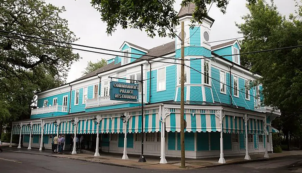 The image shows a large two-story building with a bright turquoise and white striped exterior featuring a sign that reads Commanders Palace Restaurant