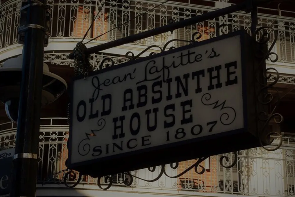The image shows a vintage-looking sign that reads Jean Lafittes Old Absinthe House Since 1807 hanging outside a building with decorative wrought-iron balconies in the background