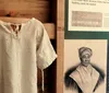 The image shows a historical exhibit featuring an old-fashioned garment on a wooden hanger and an informational poster with text and an illustration of a woman wearing a traditional headwrap called a tignon