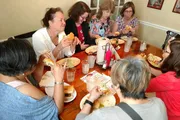 A group of people is enjoying what appears to be a casual meal together at a restaurant, with several of them eating sandwiches and all of them engaged in conversation or focused on their food.