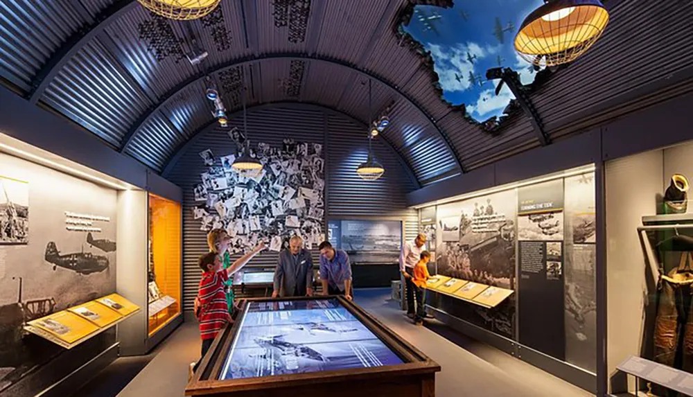 Visitors are engaged with interactive exhibits and historical displays inside a museum gallery with a corrugated metallic ceiling and dramatic lighting