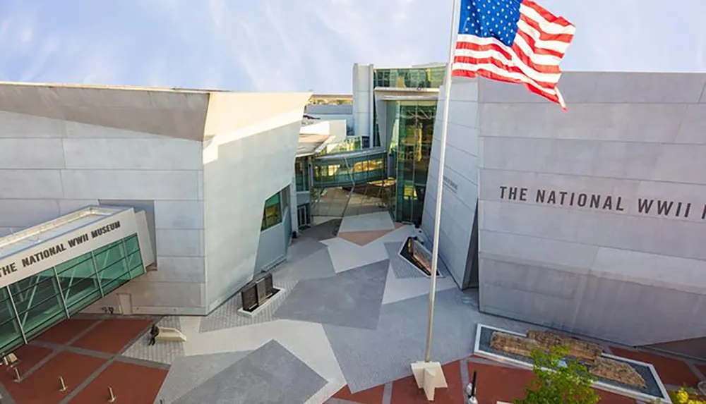 This image shows the contemporary architecture of The National WWII Museum under a clear sky with the American flag waving in front