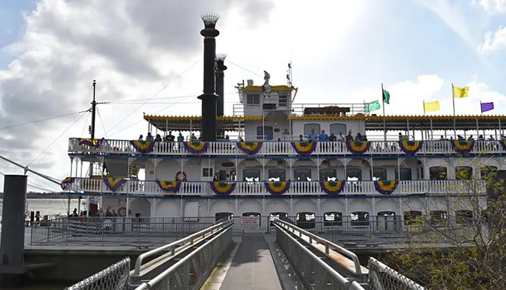 The image shows a multi-deck riverboat adorned with colorful bunting docked at a pier with people visible on its decks