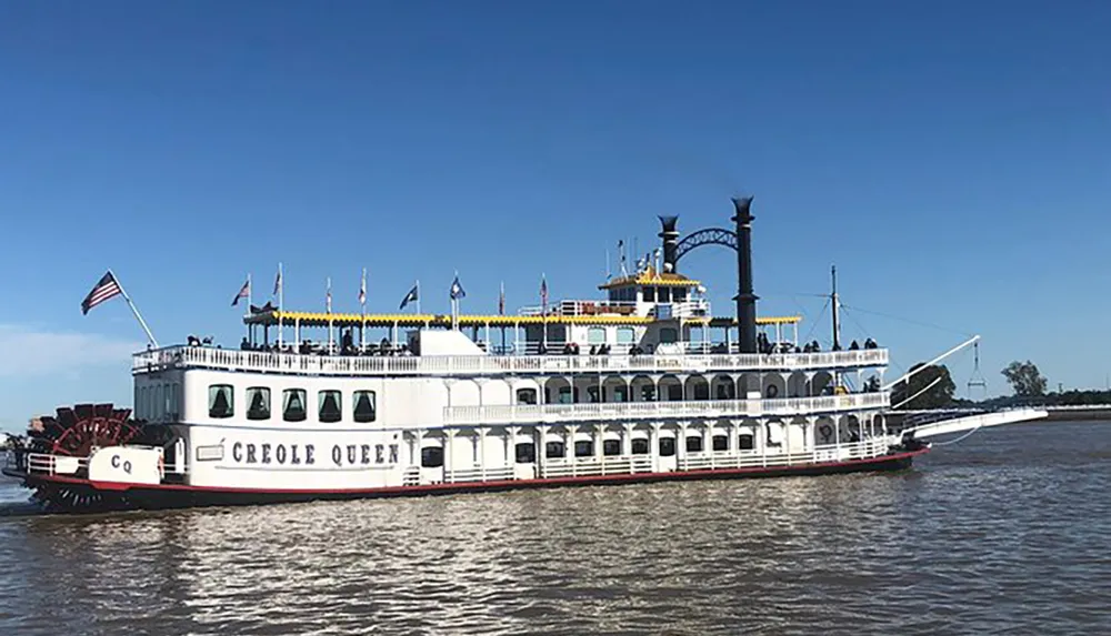 The image shows a traditional paddle-wheel riverboat named the Creole Queen on a body of water under a clear blue sky
