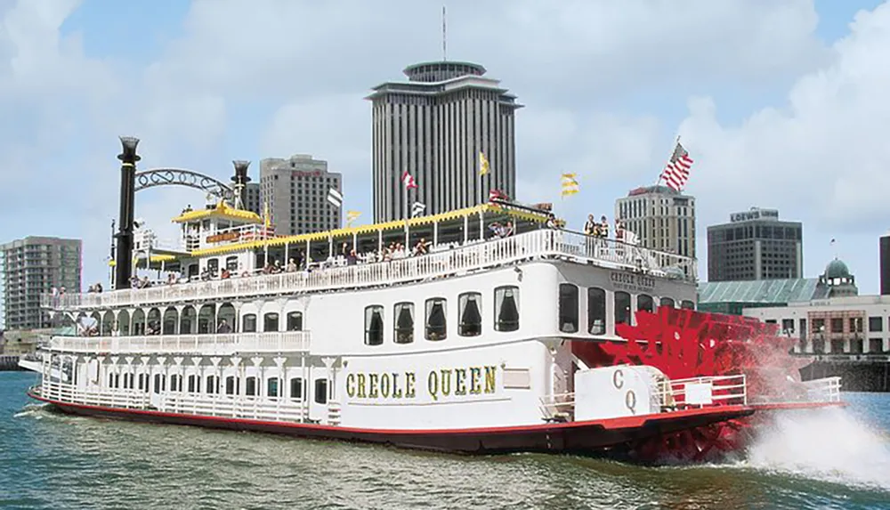A paddle-wheel riverboat named Creole Queen is cruising on the water with a cityscape in the background