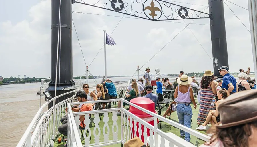 Passengers enjoy a sunny day on the deck of a paddlewheel riverboat.