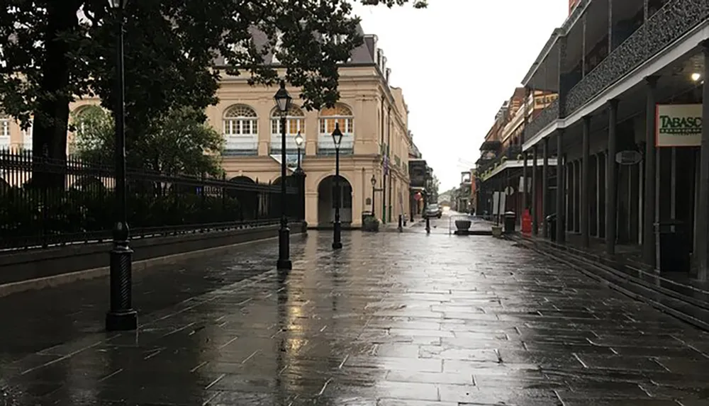 The image shows a deserted wet street flanked by historic buildings with a solitary figure walking in the distance under an overcast sky that suggests recent rain