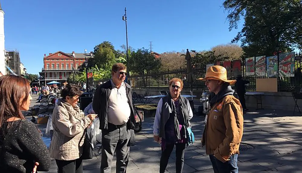 A group of people engage in conversation on a sunny day in a bustling outdoor setting with historic buildings in the background