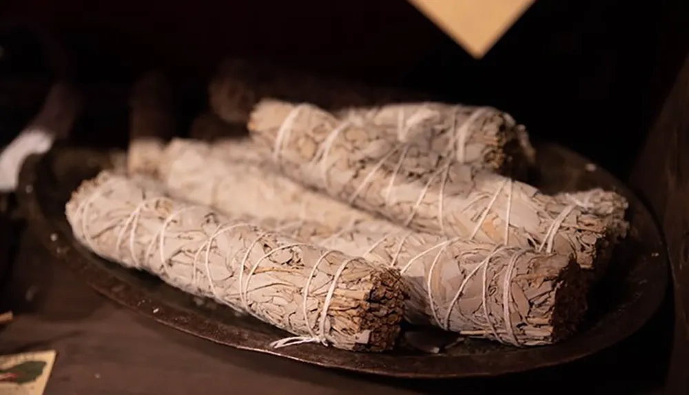 The image shows a collection of white sage smudge sticks arranged on a dark plate commonly used for cleansing rituals