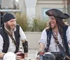 Two people dressed as pirates are laughing and enjoying themselves at a table with a bottle and pirate-themed items