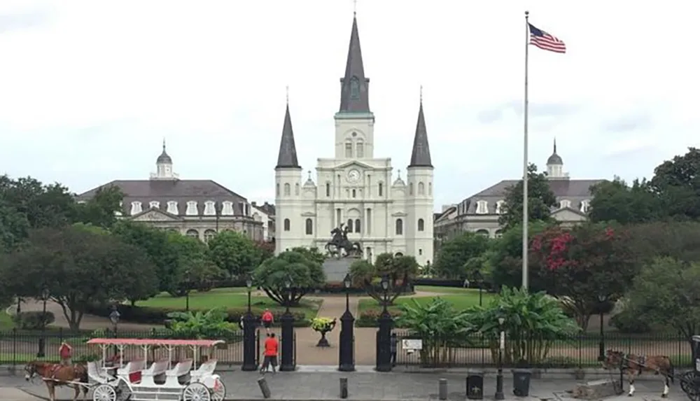 The image shows Jackson Square with the iconic St Louis Cathedral a horse-drawn carriage in the foreground and the American flag to the right possibly located in New Orleans Louisiana