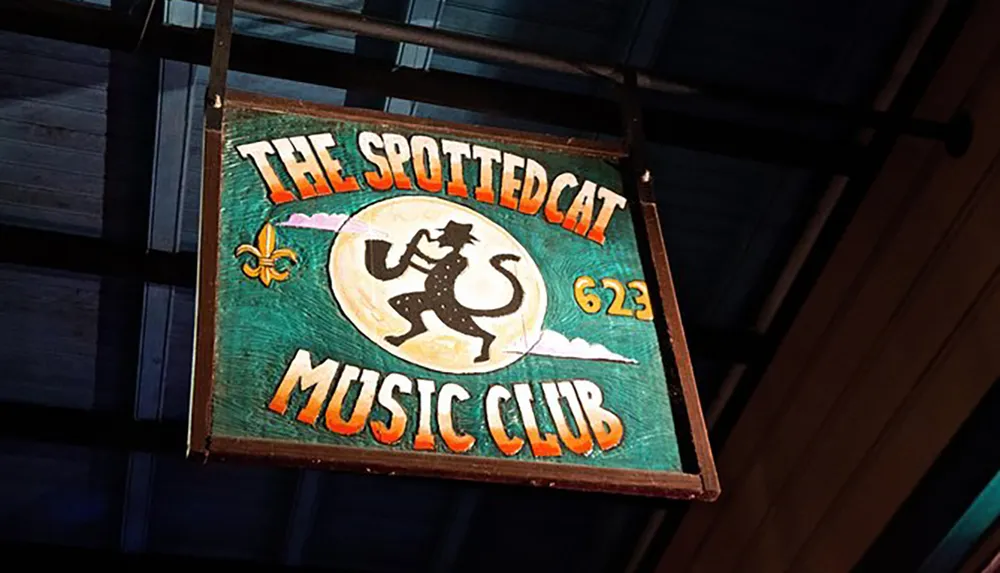 The image shows a colorful sign for The Spotted Cat Music Club featuring an illustration of a dancing cat playing a saxophone along with a fleur-de-lis symbol