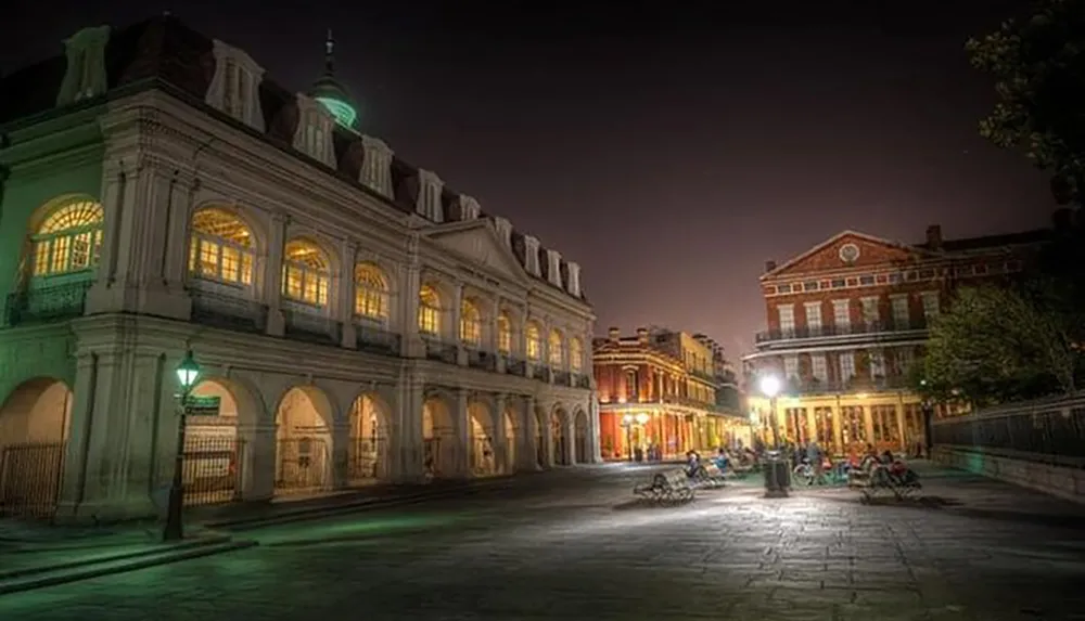 The image displays a tranquil night scene in an old well-lit historic town square with classical architecture and a few people sitting on benches