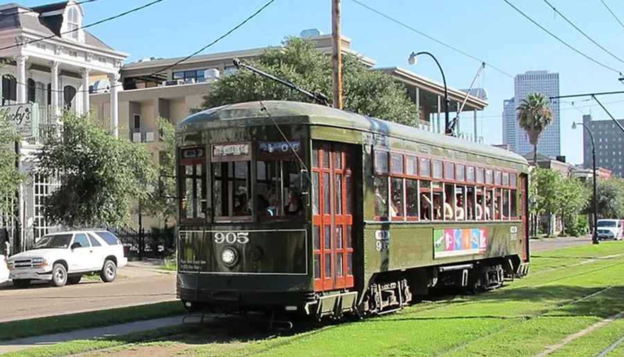 A green vintage streetcar is traveling along a city track, with passengers visible inside, set against a backdrop of urban buildings and clear skies.