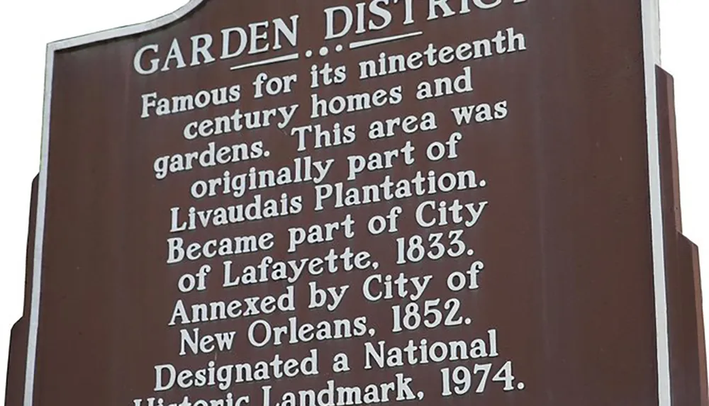The image shows a historical marker for the Garden District detailing its fame for nineteenth-century homes and gardens its origins as part of the Livaudais Plantation and its annexations by the City of Lafayette in 1833 and by the City of New Orleans in 1852 concluding with its designation as a National Historic Landmark in 1974