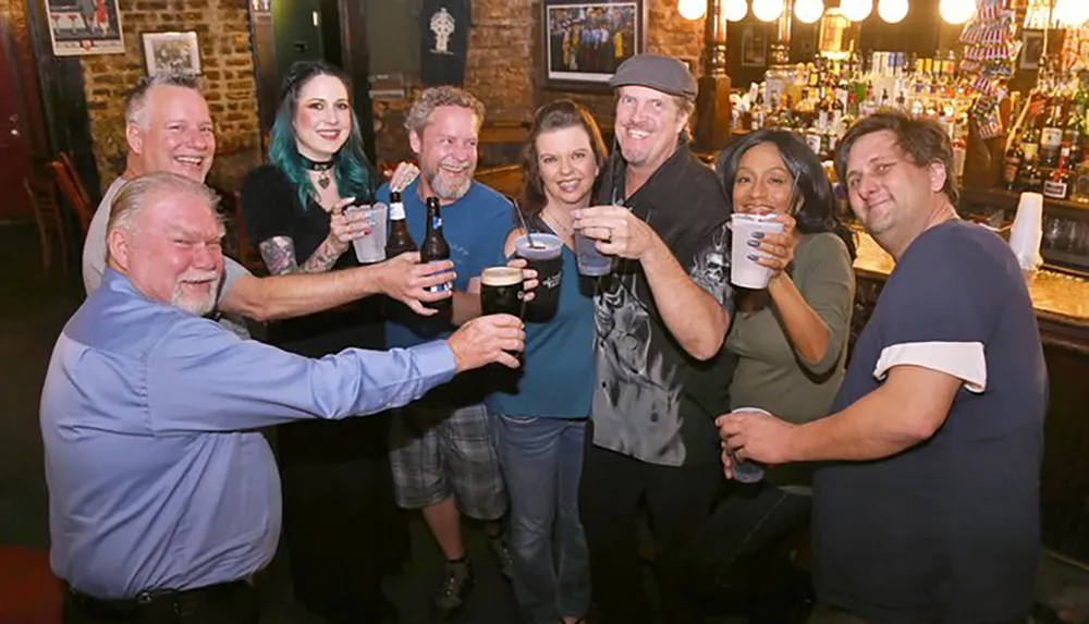 A group of eight people is smiling and toasting with various drinks at a bar
