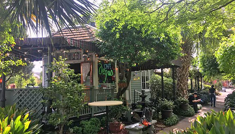 A quaint café with outdoor seating is nestled among lush greenery and string lights, creating a cozy atmosphere.