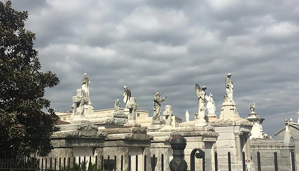 This image shows a collection of statues on top of stone structures under a cloudy sky possibly located in a cemetery or memorial park