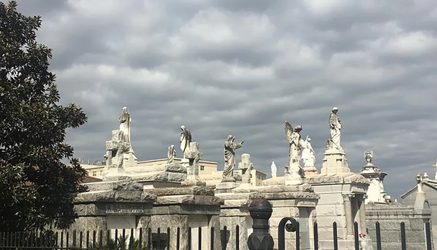 This image shows a collection of statues on top of stone structures under a cloudy sky, possibly located in a cemetery or memorial park.