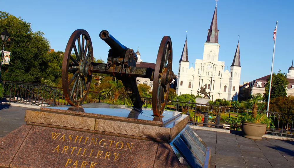 An old cannon is displayed at Washington Artillery Park with the iconic St Louis Cathedral in the background under a clear blue sky