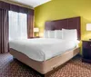 This is a neatly arranged hotel room with a large bed bright yellow walls and patterned curtains and carpet