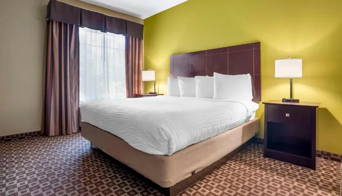 This is a neatly arranged hotel room with a large bed bright yellow walls and patterned curtains and carpet