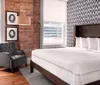 The image shows a stylish bedroom with a large bed exposed brick wall elegant grey armchair and decorative silhouette portraits exuding a modern yet cozy atmosphere