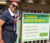 A woman is posing next to a sign that reads Flooded House Museum at the breach site of London Avenue Canal Floodwall in New Orleans