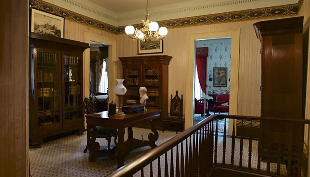 The image shows a warmly lit Victorian-style study room with a bookcase desk and antique furnishings viewed from an adjoining room through an open doorway