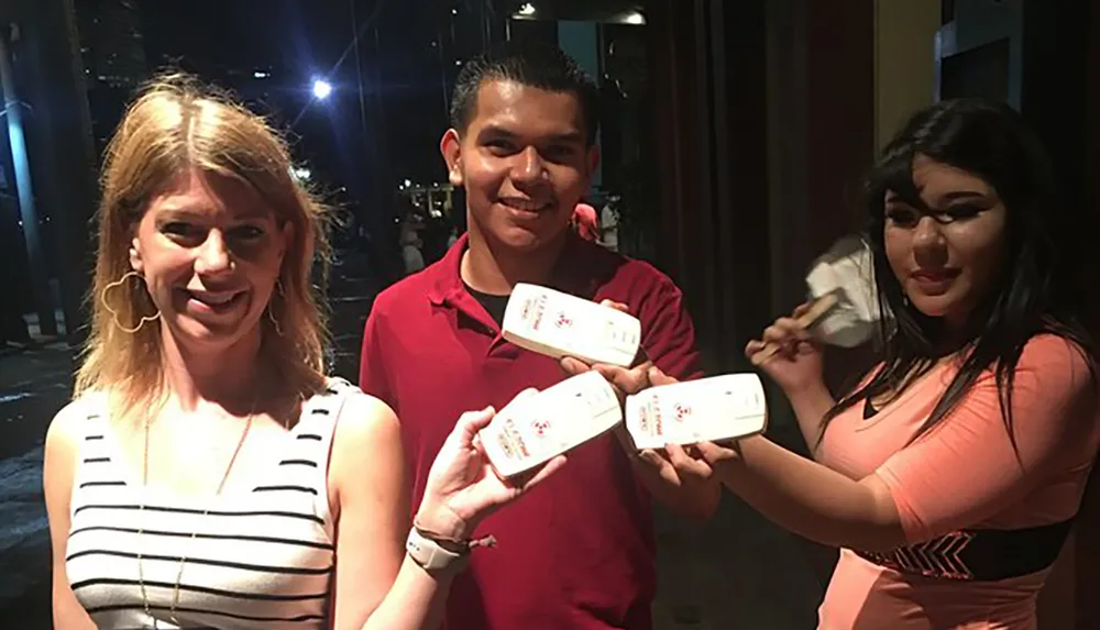 Three people are smiling and holding tickets or vouchers of some sort in a night-time setting
