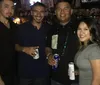 Four people are smiling for a photo while standing together in a bar setting with some holding cans of beer