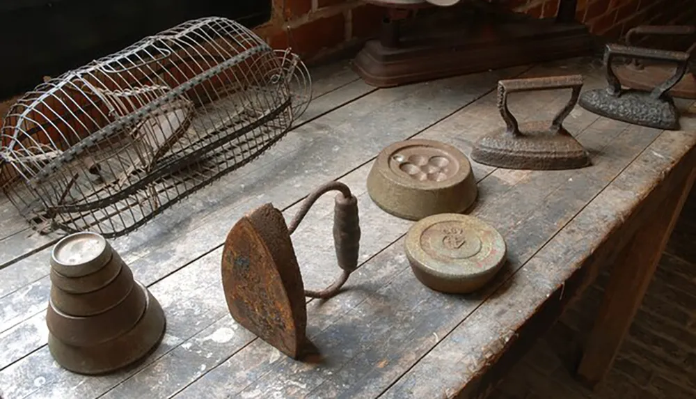 This image shows a collection of vintage household items including two irons a birdcage and some weights displayed on a rustic wooden table