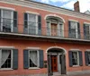 The image shows a two-story red brick building with a balcony gray shutters and a white cornice reflecting a typical architectural style found in the French Quarter of New Orleans